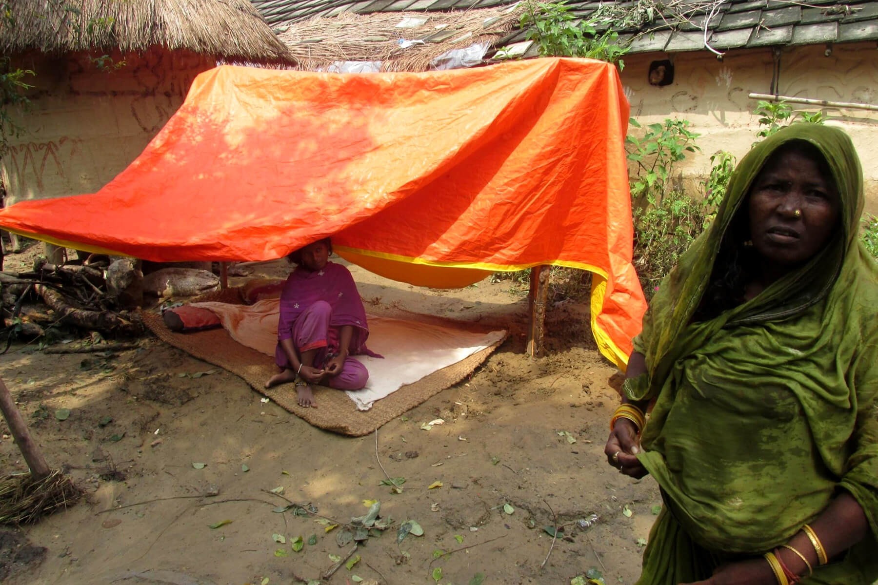 Flood affected women stay under a makeshift tarpaulin shelter in Parsa district